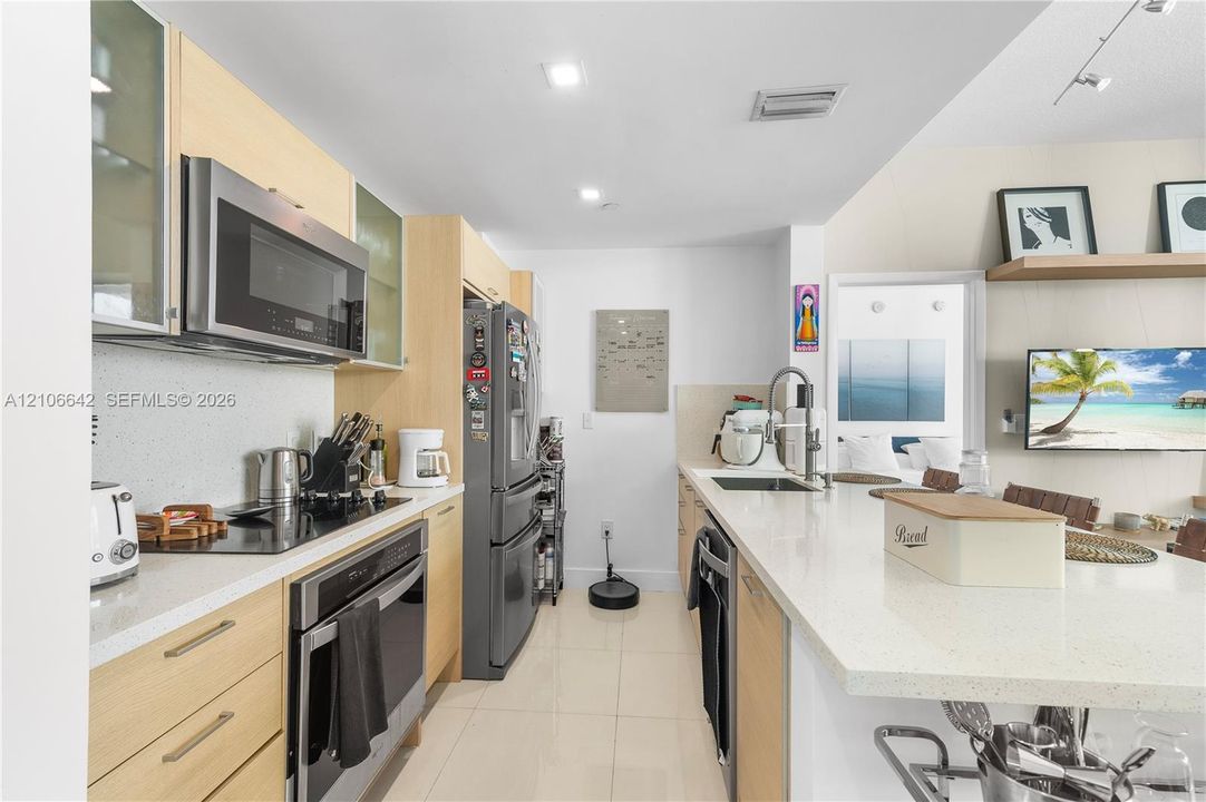 Kitchen featuring light wood-finish cabinetry, stone-style countertops, stainless steel appliances, recessed lighting, and a breakfast bar