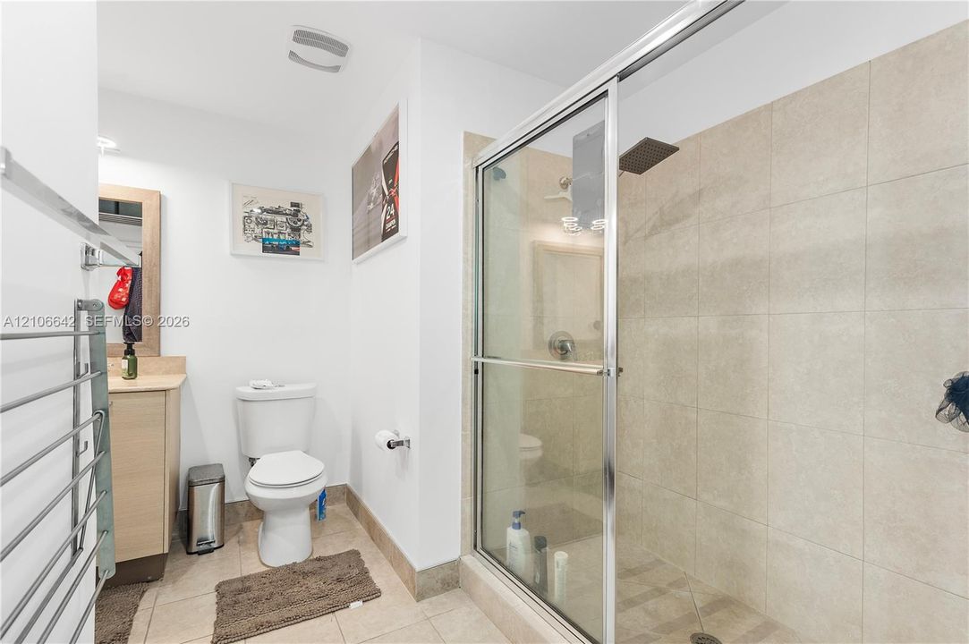 Second bathroom featuring a shower stall with tile surround, glass sliding door, and a fixed showerhead, complemented by a wood-finish vanity and neutral tile flooring