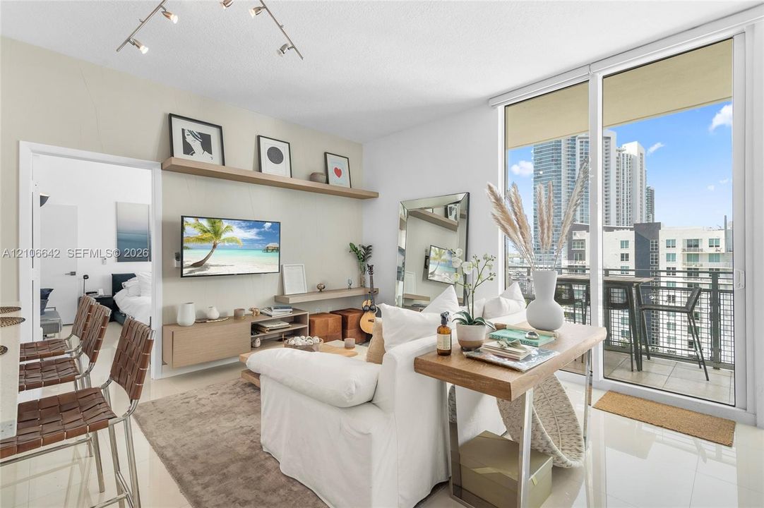 Living area featuring floor-to-ceiling glass sliding doors, polished tile flooring, built-in wall-mounted shelving, and a balcony with metal railing