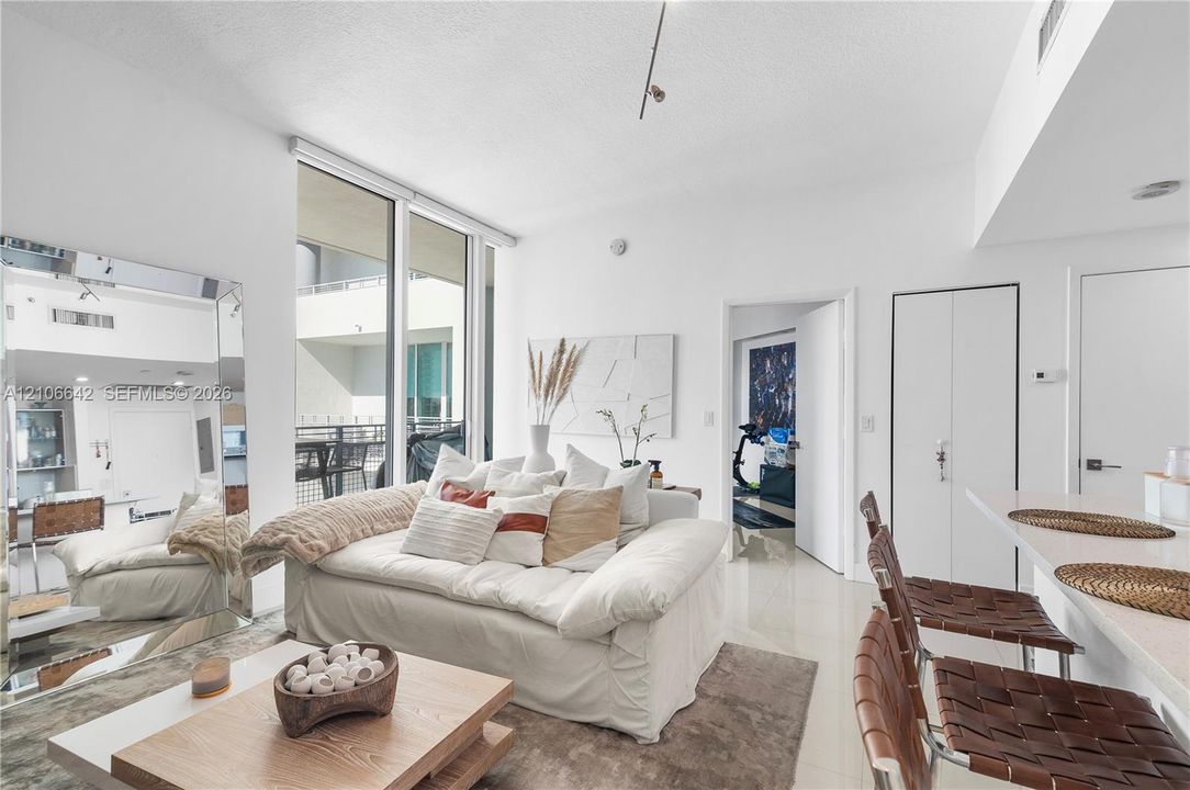 Open-concept living area featuring floor-to-ceiling windows, neutral tile flooring, track lighting, and a breakfast bar with stone-finish countertops
