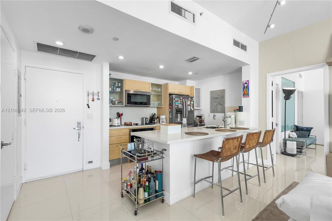 Kitchen featuring light wood-finish cabinetry, quartz countertops, a central island with integrated sink, recessed lighting, and tile flooring
