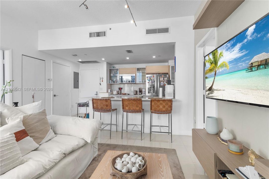 Open-concept interior featuring high-gloss tile flooring, recessed ceiling lighting, a breakfast bar with stone-finish countertops, and built-in wall cabinetry