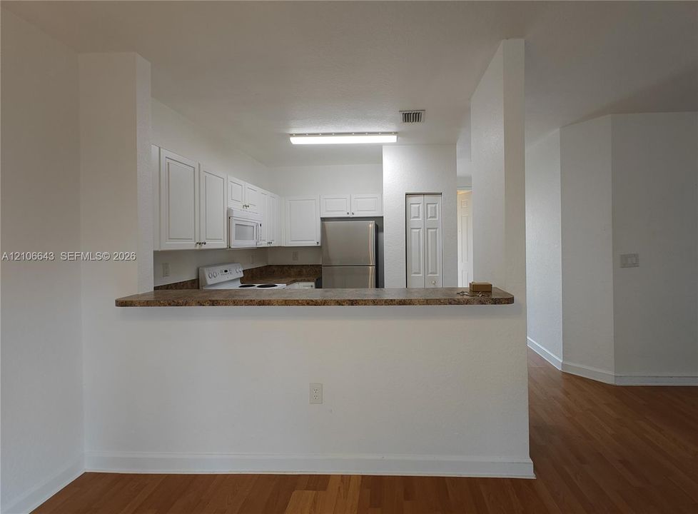 Kitchen featuring white cabinetry, solid-surface countertops, a stainless steel refrigerator, a built-in microwave, and a double-door pantry