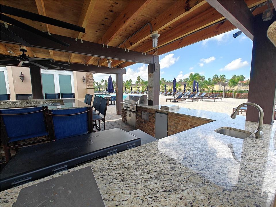 Outdoor recreational area featuring an artificial turf surface, a permanent playground structure, a black metal perimeter fence, and direct exterior access to a swimming pool