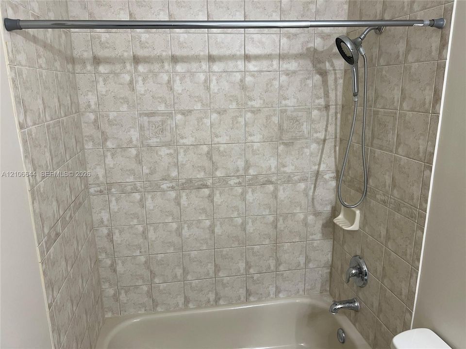 Full-height ceramic tile shower surround, integrated soap dish, chrome handheld shower head, and porcelain bathtub