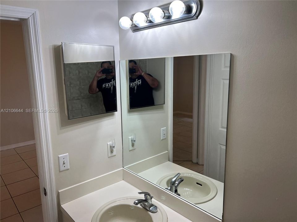 Wall-mounted medicine cabinet with a mirrored door, large rectangular wall mirror, vanity countertop with an integrated sink, polished chrome faucet, and multi-bulb vanity light fixture