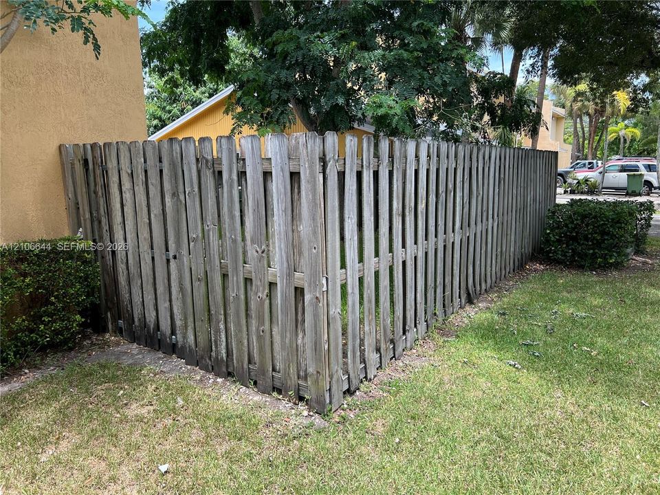 Vertical wood picket fencing enclosing a grass lawn with mature trees and perimeter shrubbery