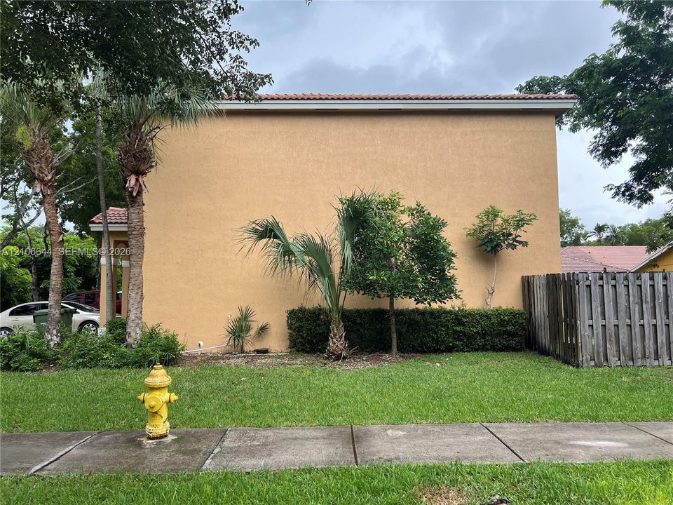 Stucco exterior featuring a tile roof, mature palm trees, integrated landscaping, and a wood privacy fence