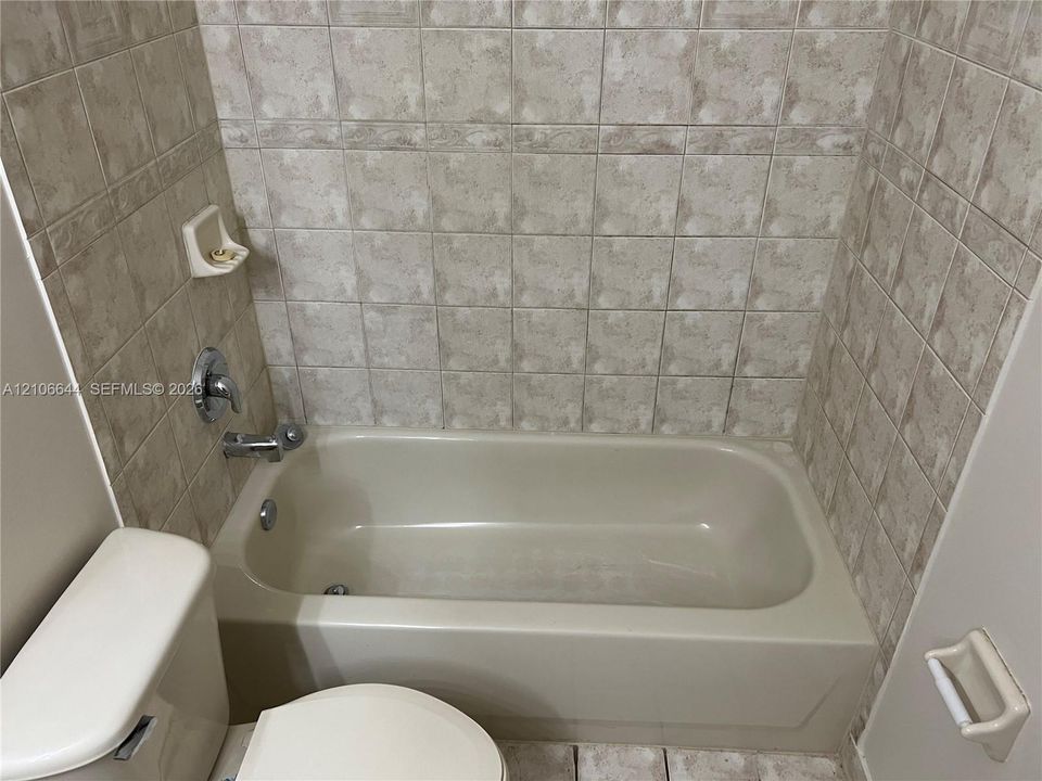 Bathtub surround featuring neutral-toned tile, built-in soap dish, and polished chrome faucet and shower hardware