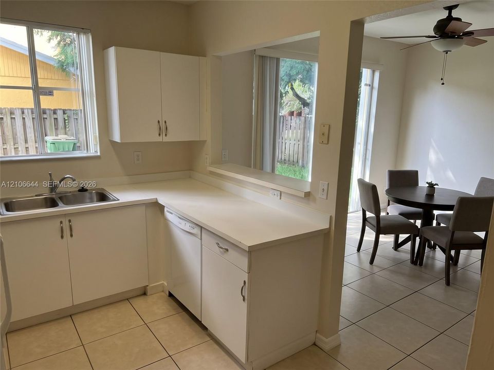 Kitchen featuring white cabinetry, solid surface countertops, stainless steel double-basin sink, and ceramic tile flooring