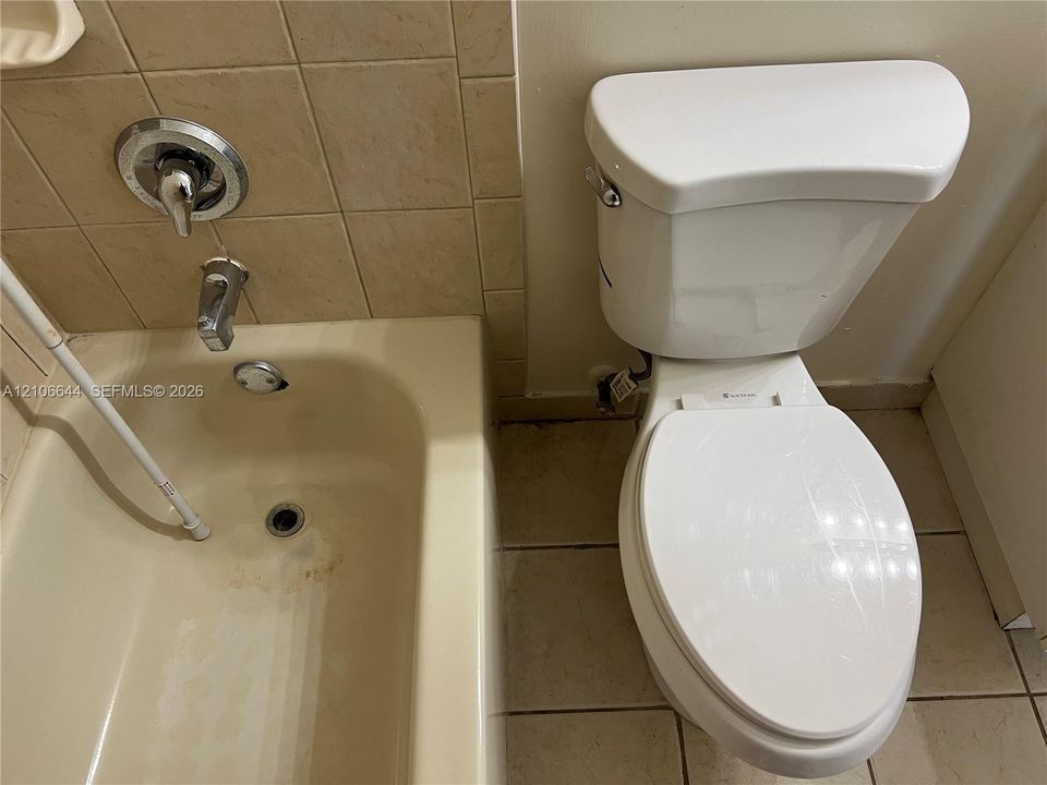 Bathroom featuring a porcelain toilet and a bathtub with a chrome single-handle mixing valve and spout, accented by tiled wall surrounds and floor tiling