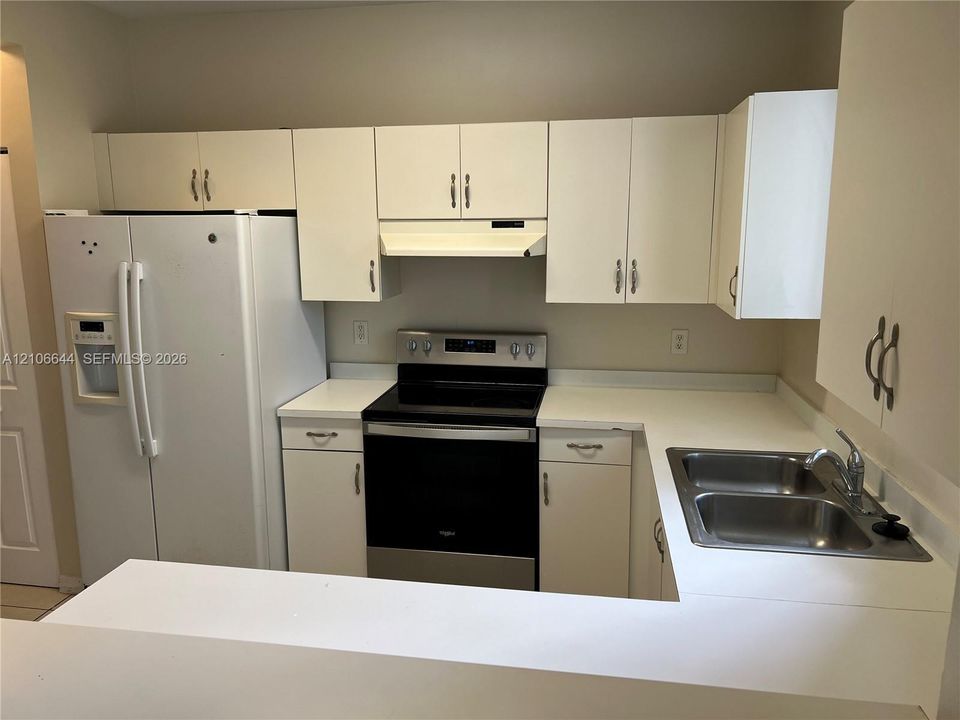 Kitchen featuring white cabinetry, solid-surface countertops, dual-basin stainless steel sink, and integrated range hood