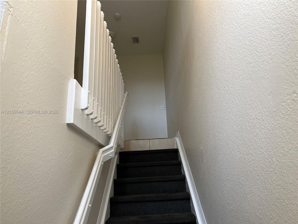 Staircase featuring dark carpeted treads and white painted vertical balustrades with a matching handrail