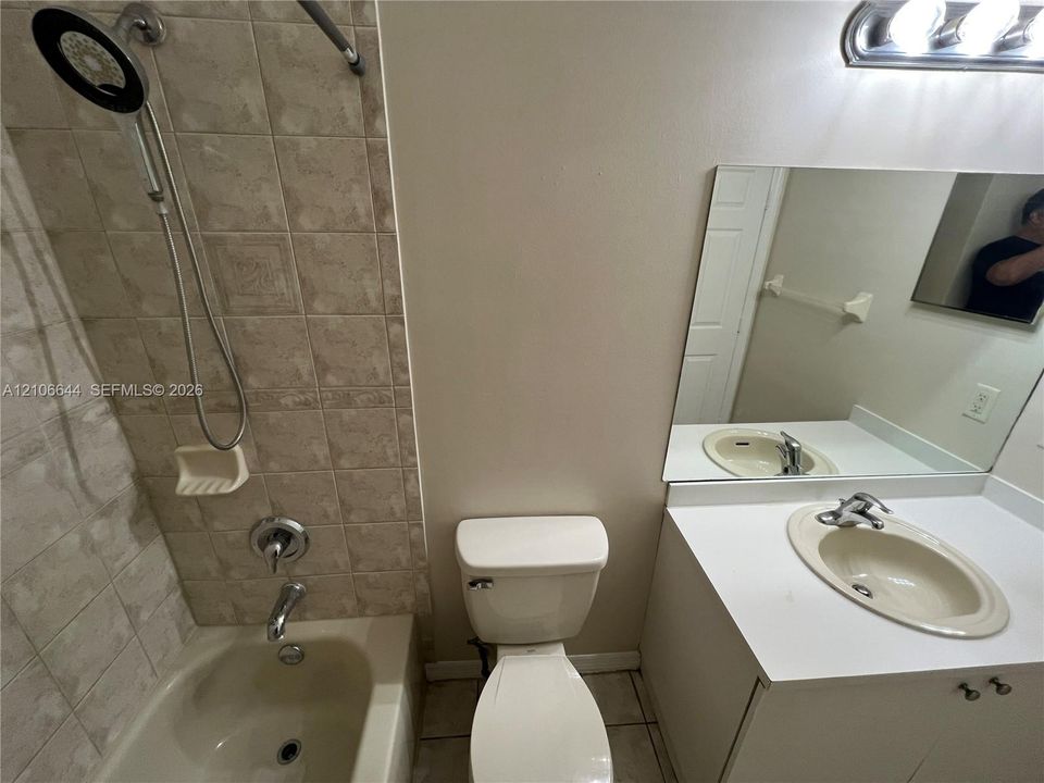 Bathroom featuring a tub-shower combination with ceramic tile surround, integrated vanity with a solid-surface countertop and drop-in basin, large wall-mounted mirror, and multi-bulb vanity light fixture