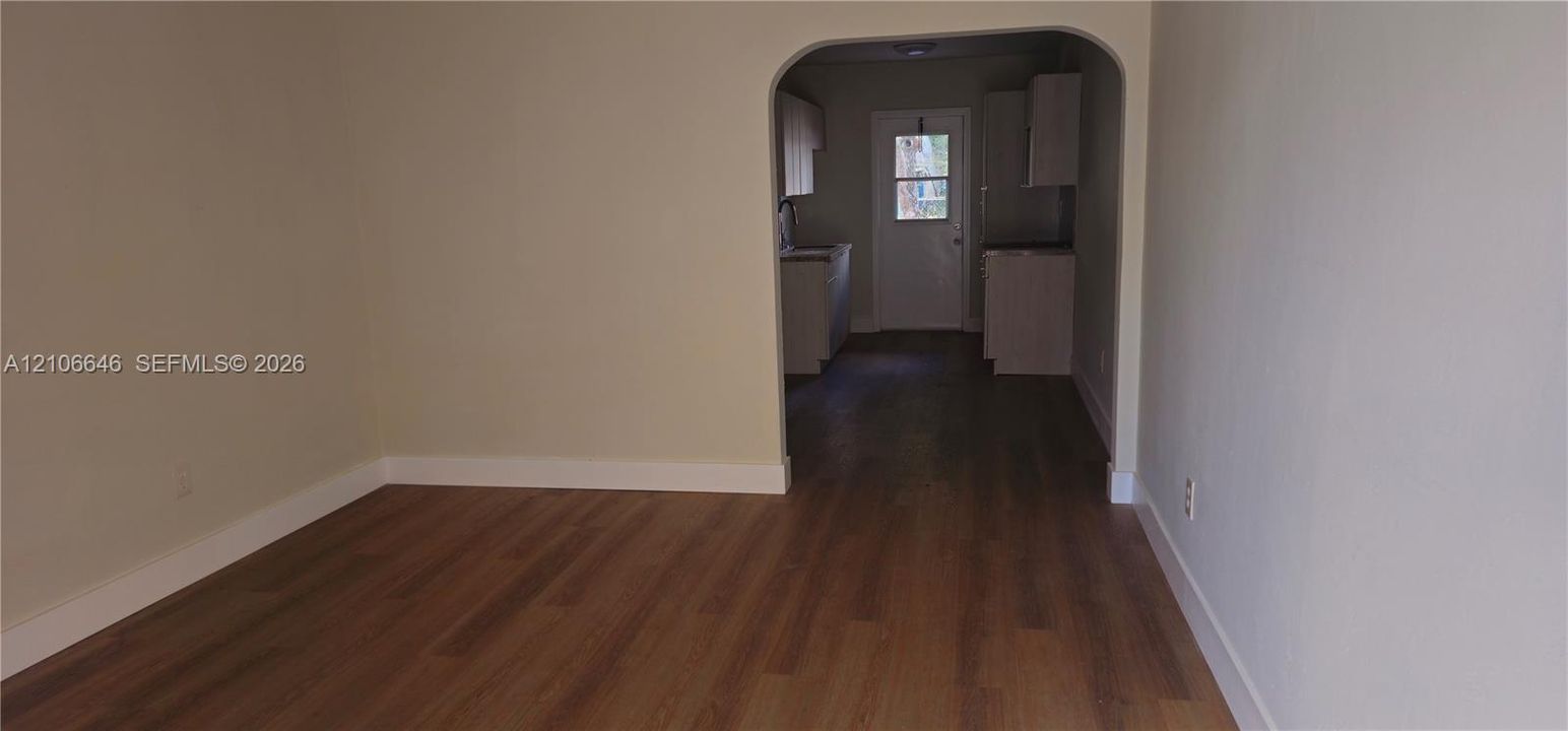 Interior space featuring wood-finish flooring, neutral wall paint, and an arched entryway leading to cabinetry and a glass-paneled exterior door