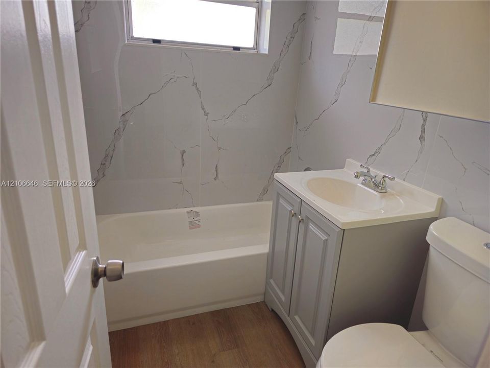 Full-height wall tiling featuring a veined pattern, wood-finish flooring, shaker-style vanity cabinet with a integrated sink, and an alcove bathtub