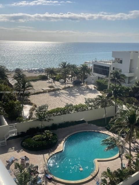 Free-form swimming pool with paved surround, lush perimeter landscaping, and direct access to sand-covered grounds