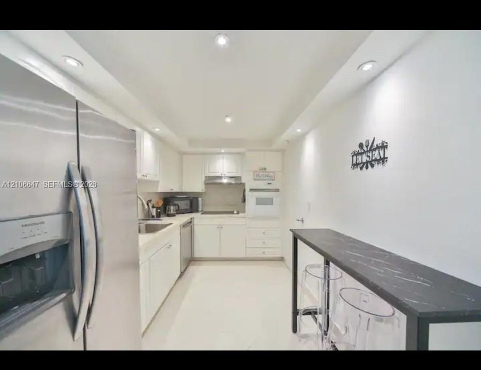 Kitchen featuring white shaker cabinetry, stainless steel refrigerator, recessed lighting, and a dark surface breakfast bar