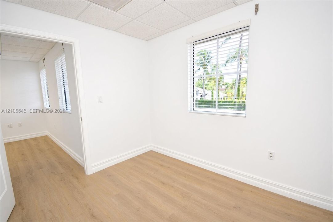 Room featuring light-toned wood-finish flooring, suspended acoustic ceiling tiles, and window blinds
