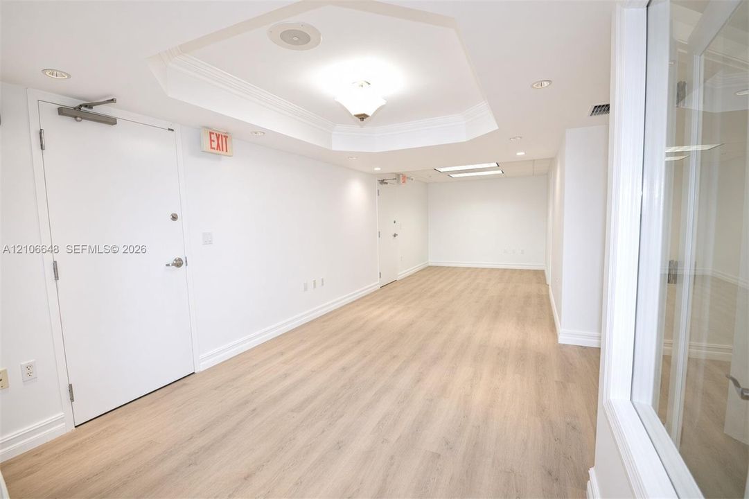 Interior space featuring light-toned wood-finish flooring, recessed ceiling lighting, a tray ceiling detail, and integrated glass paneling