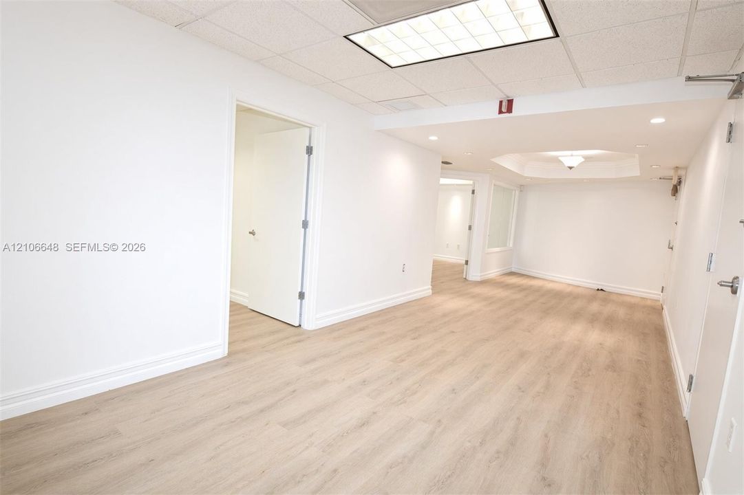 Open floor plan featuring wood-finish flooring, recessed lighting, a coffered ceiling detail, and a drop ceiling with a panel light fixture