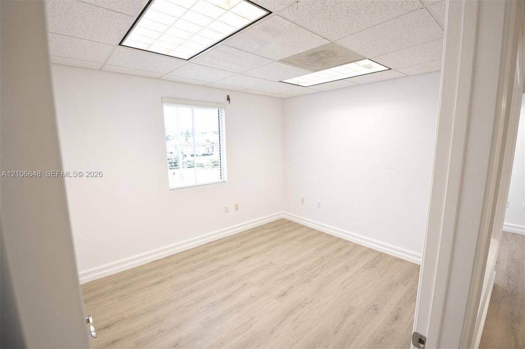 Room featuring light-toned wood-finish flooring, white walls, recessed ceiling lighting, and a single-pane window