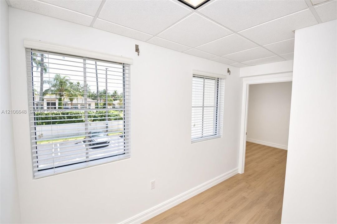 Interior space featuring wood-finish flooring, two windows with horizontal blinds, and a drop ceiling