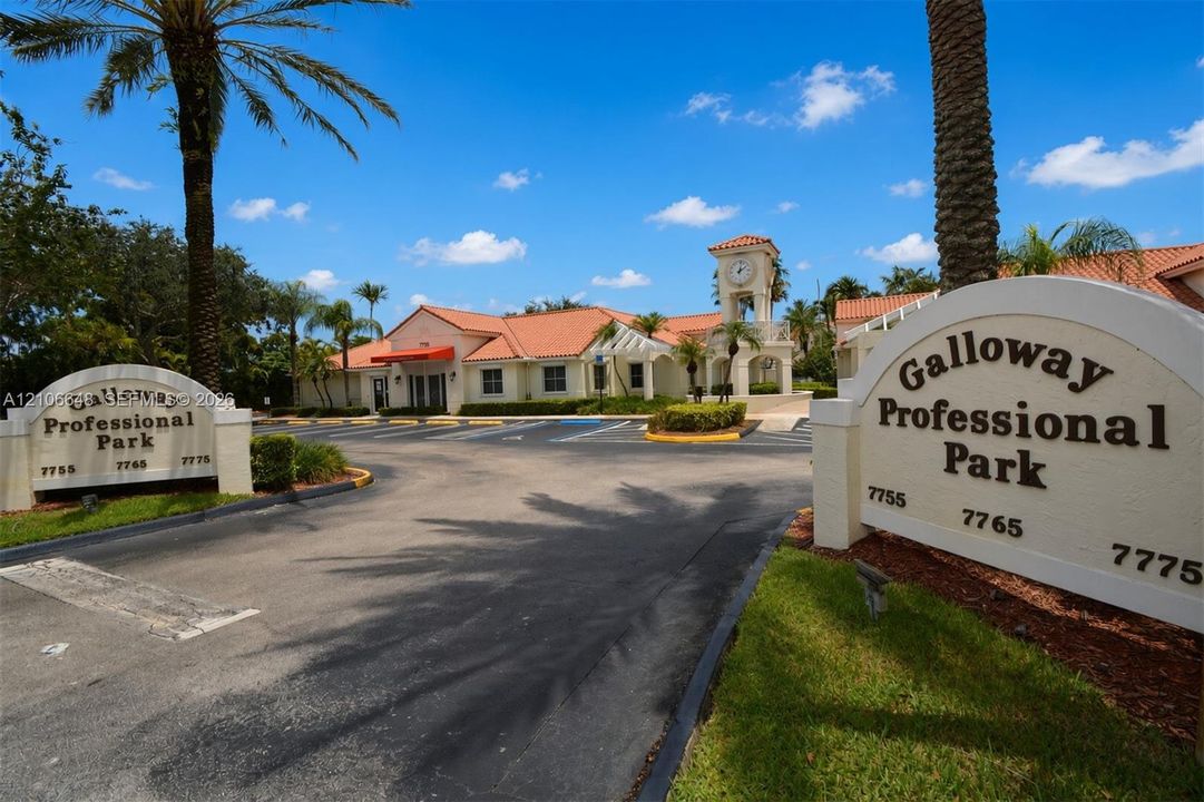 Galloway Professional Park exterior featuring a stucco clock tower, terracotta-style roof tiles, paved parking area, and landscaped grounds with mature palm trees