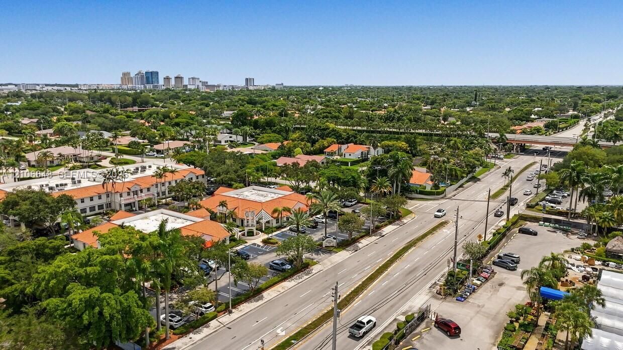 Aerial perspective of a multi-building complex featuring clay tile roofing, manicured palm trees, and paved surface parking