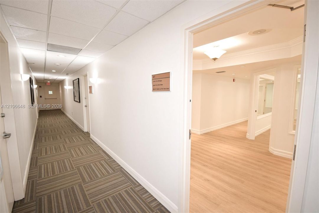 Hallway featuring grid-pattern carpet, suspended drop ceiling, recessed lighting, wall-mounted sconces, and wood-finish flooring