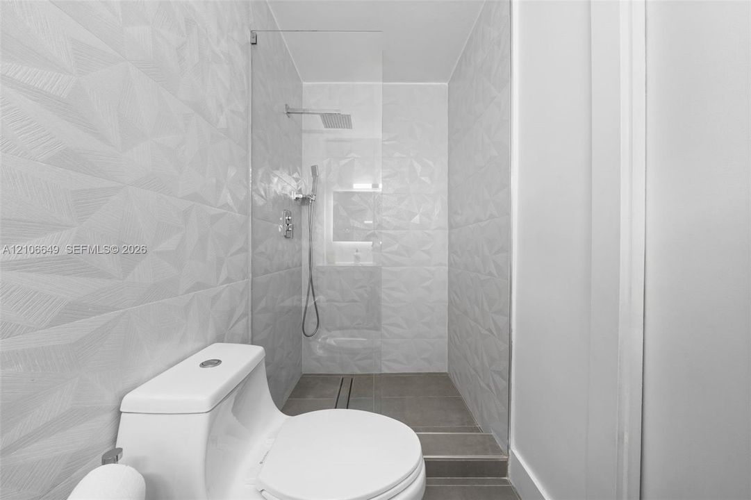 Walk-in shower featuring textured geometric wall tile, a frameless glass enclosure, a rainfall showerhead, and a built-in recessed niche