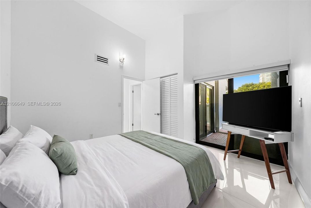 Vaulted ceilings, large sliding glass doors, white tiled flooring, and louvered closet doors