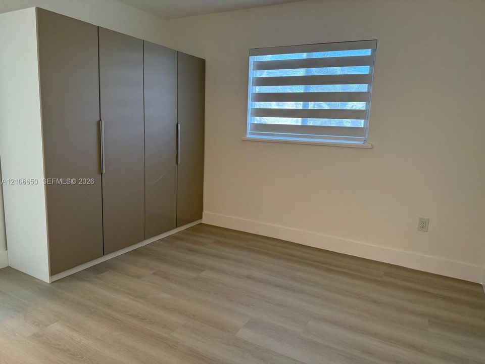 Built-in floor-to-ceiling cabinetry with metallic finish, wood-finish flooring, and window with banded roller shade