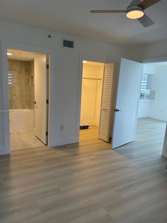 Wood-finish flooring, ceiling fan with integrated lighting, bathroom featuring a tiled shower enclosure, and reach-in closet with louvered doors