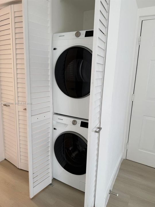 Stacked laundry center featuring high-efficiency front-load appliances enclosed by white louvered bi-fold doors