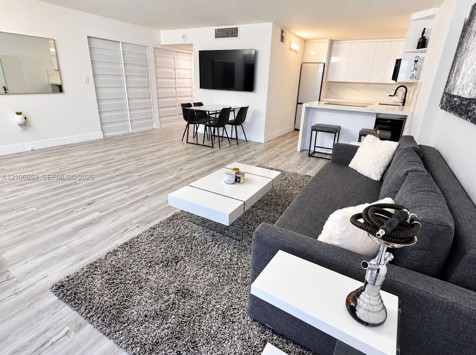 Open-concept interior featuring light wood-finish flooring, high-gloss white cabinetry, white countertops with integrated breakfast bar, and recessed lighting