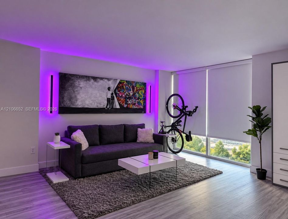 Living area featuring wood-finish flooring, floor-to-ceiling windows with roller shades, integrated cove lighting, and dual vertical wall-mounted fixtures