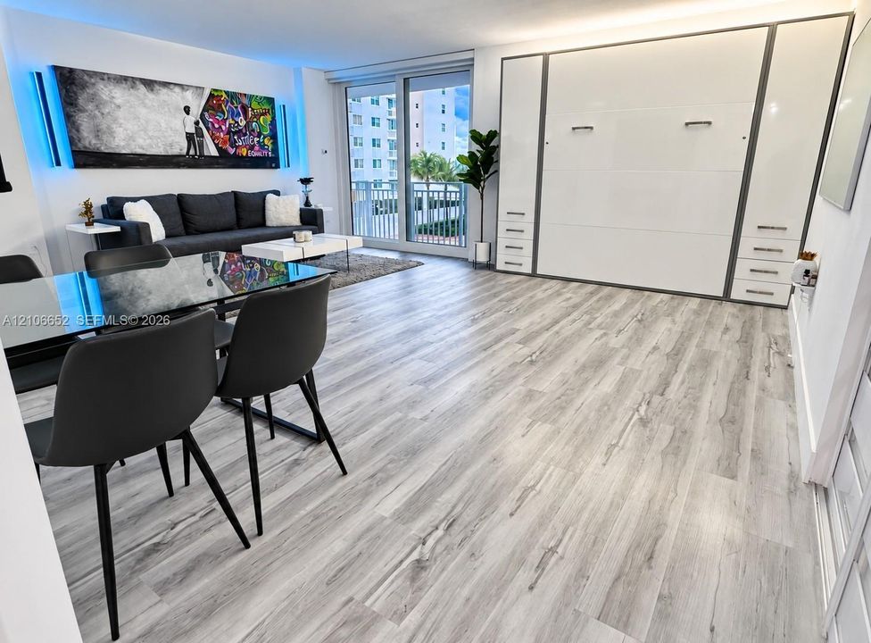 Open-concept living space featuring wood-finish flooring, floor-to-ceiling built-in cabinetry, and a large sliding glass door providing external access to a balcony