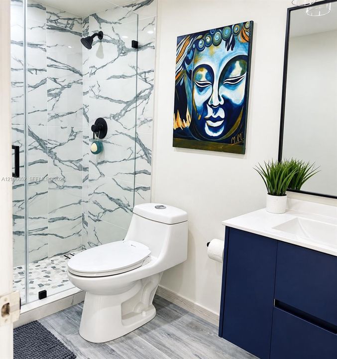 Bathroom featuring a glass-enclosed shower with vein-patterned wall tile and stone-style floor tile, a navy blue vanity cabinet with a white countertop, and a matte black framed mirror