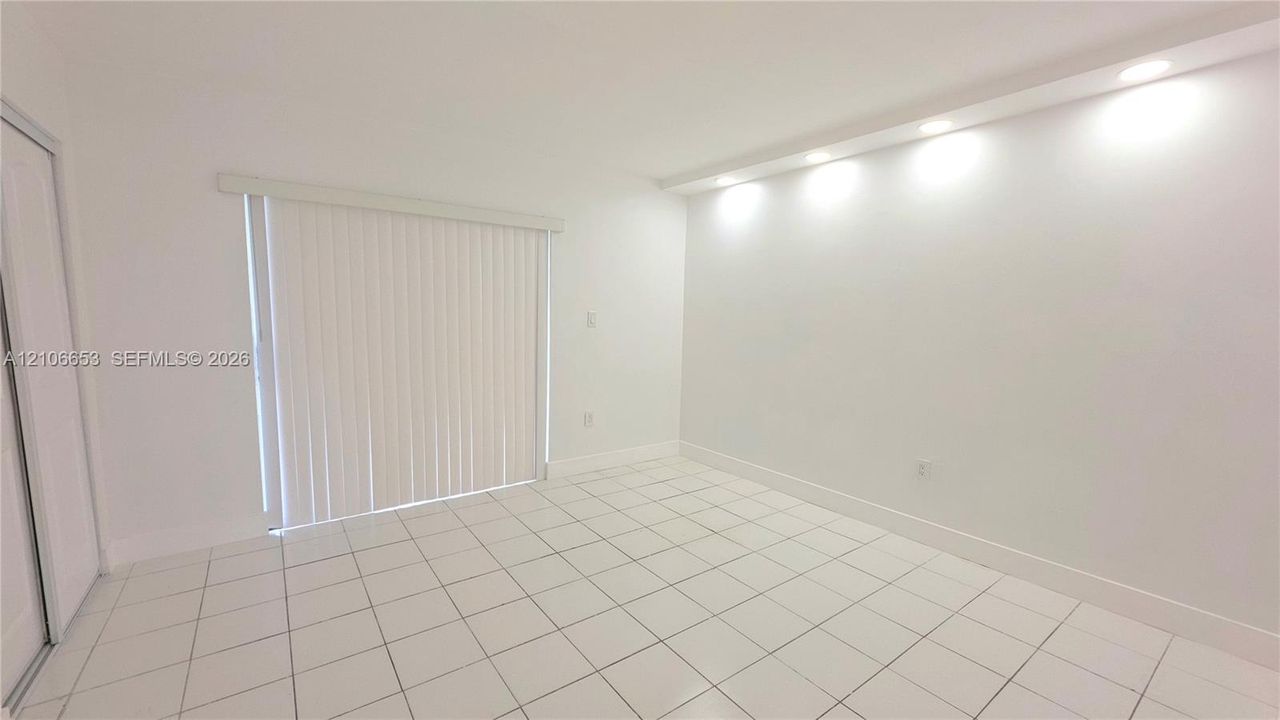 Bright room featuring white ceramic tile flooring, recessed cove lighting, and sliding glass doors with vertical blinds