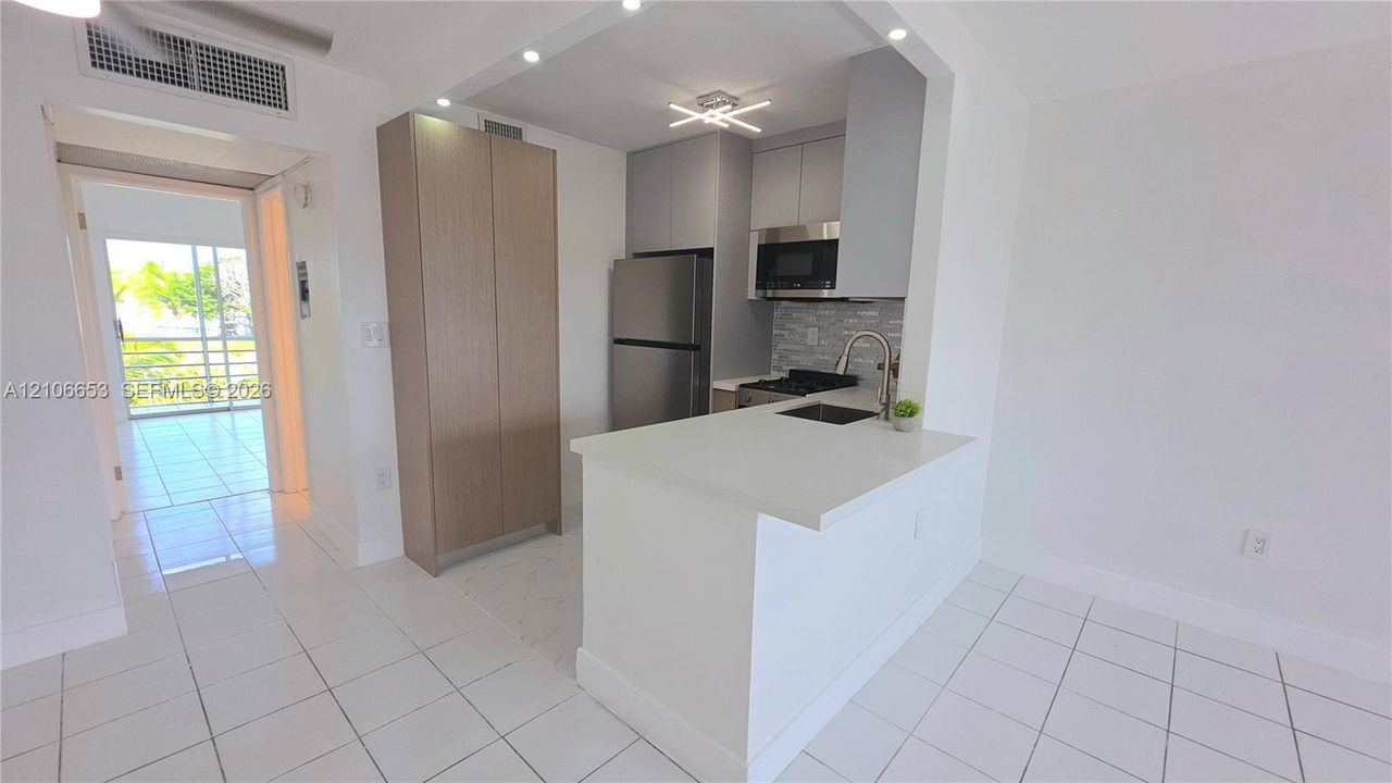 Kitchen featuring stainless steel appliances, neutral cabinetry, quartz-finish countertops, tiled flooring, and a breakfast bar