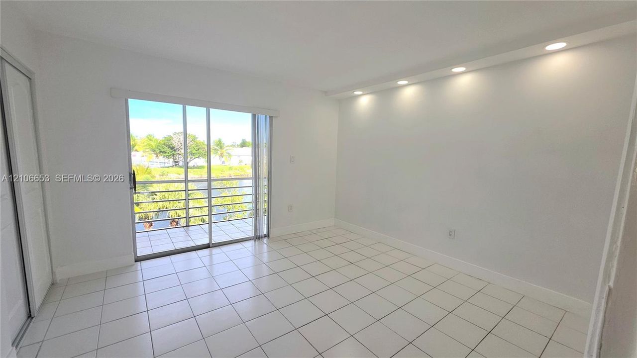 Room with large format white tile flooring, recessed cove lighting, and sliding glass doors opening to a balcony with metal railing