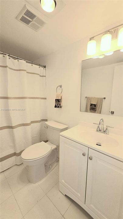 Bathroom featuring a white vanity cabinet with a integrated sink, polished chrome faucet, large rectangular mirror, and an overhead multi-bulb lighting fixture