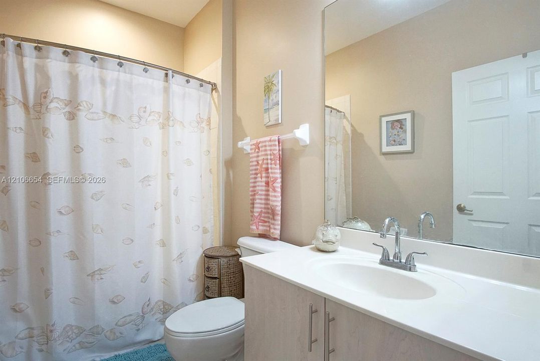 Vanity featuring a solid surface countertop, integrated oval sink, and chrome-finish dual-handle faucet, paired with a large wall-mounted mirror and shower-tub combination