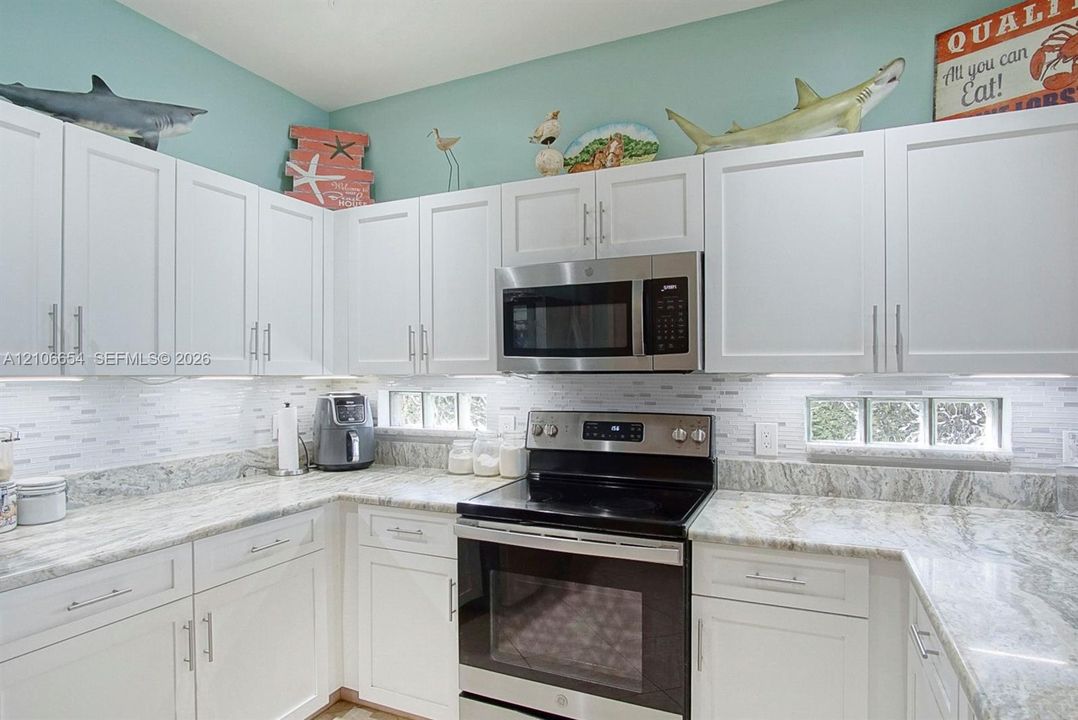 Kitchen featuring white shaker-style cabinetry, stone countertops, stainless steel appliances, and a horizontal glass block backsplash