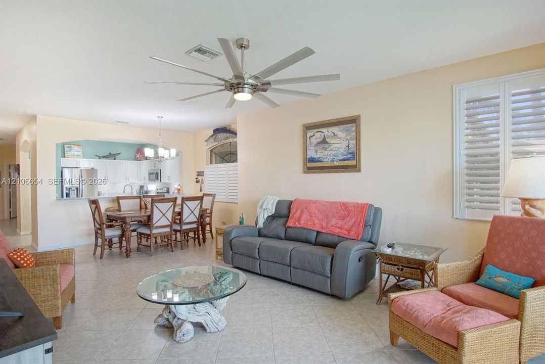 Living area featuring tile flooring, multi-blade ceiling fan, arched wall cut-out, and white plantation shutters