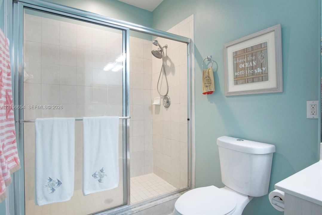 Walk-in shower with a chrome-finished sliding glass door, white tile surround, and adjustable handheld showerhead