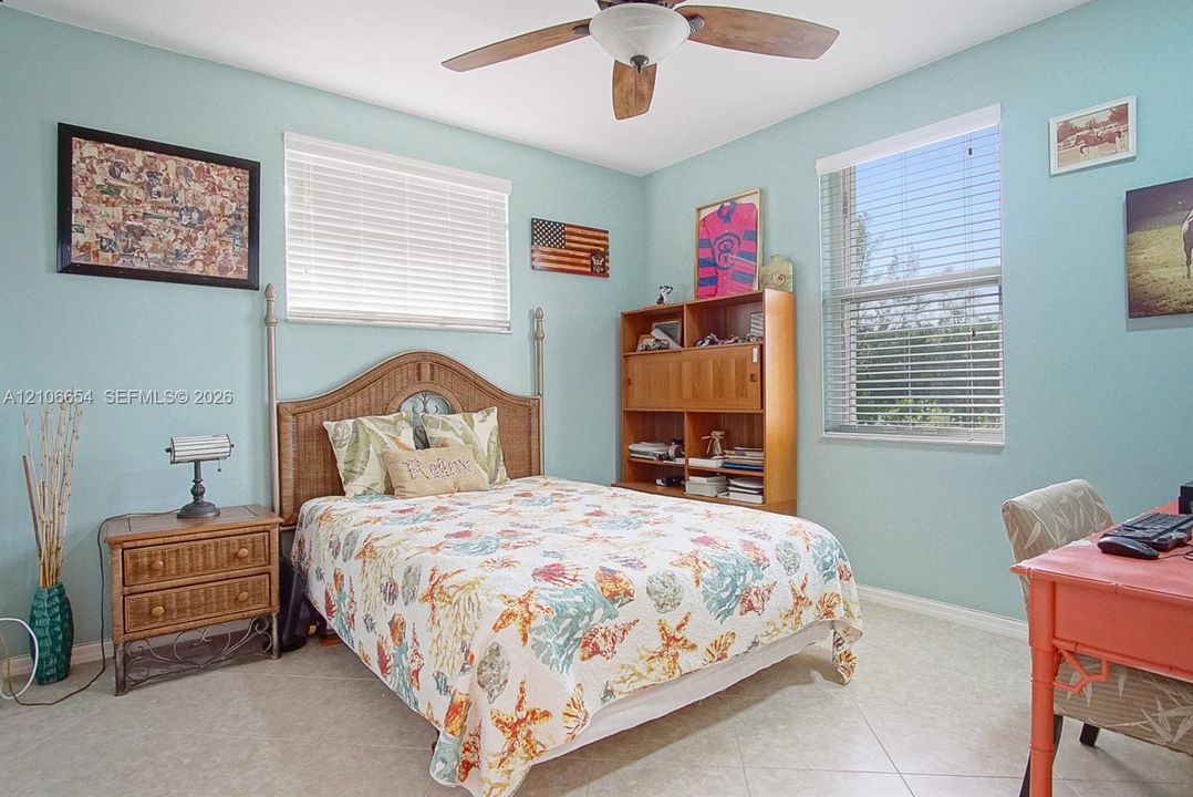 Bedroom featuring neutral tile flooring, dual windows with horizontal blinds, and a central ceiling fan with integrated lighting