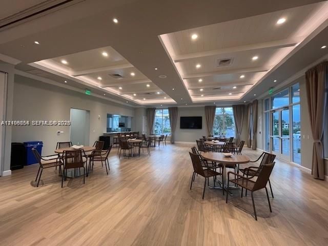 Expansive interior space featuring wood-finish flooring, tray ceilings with recessed lighting, floor-to-ceiling glass doors, and a built-in service counter
