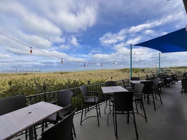 Covered outdoor terrace featuring a concrete floor, black metal railing, overhead string lighting, and a blue shade canopy overlooking coastal dunes